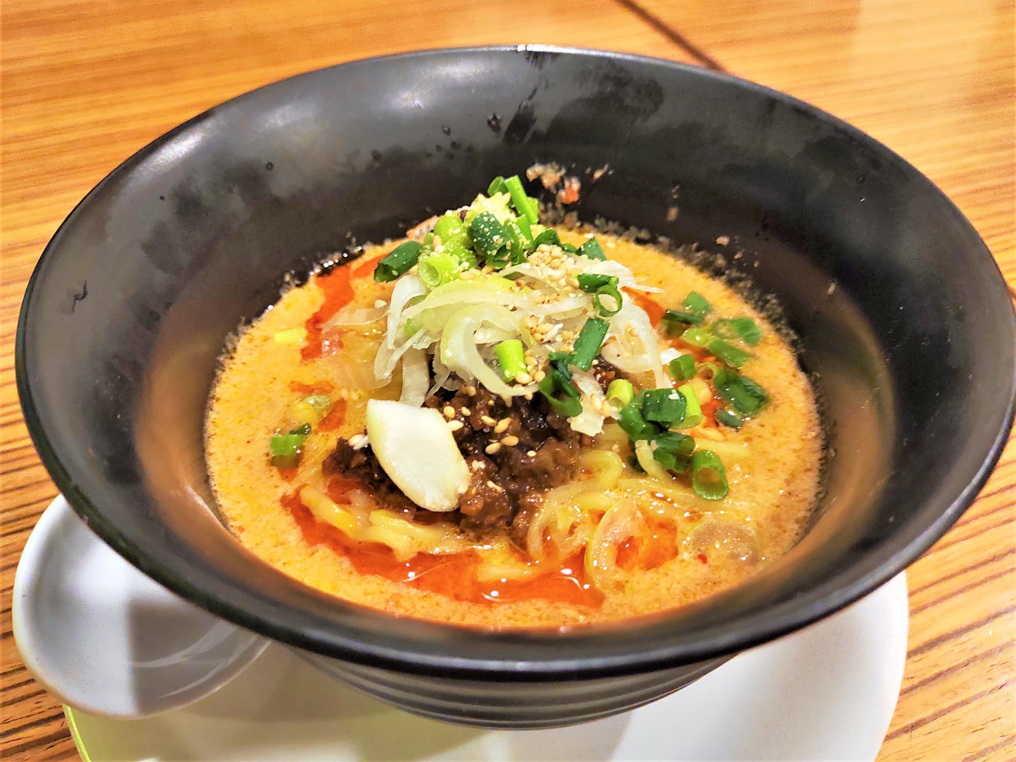 白胡麻担々麺のアップ写真。濃い色のスープに白ねぎ、青ねぎ、細切り野菜がのった一杯。