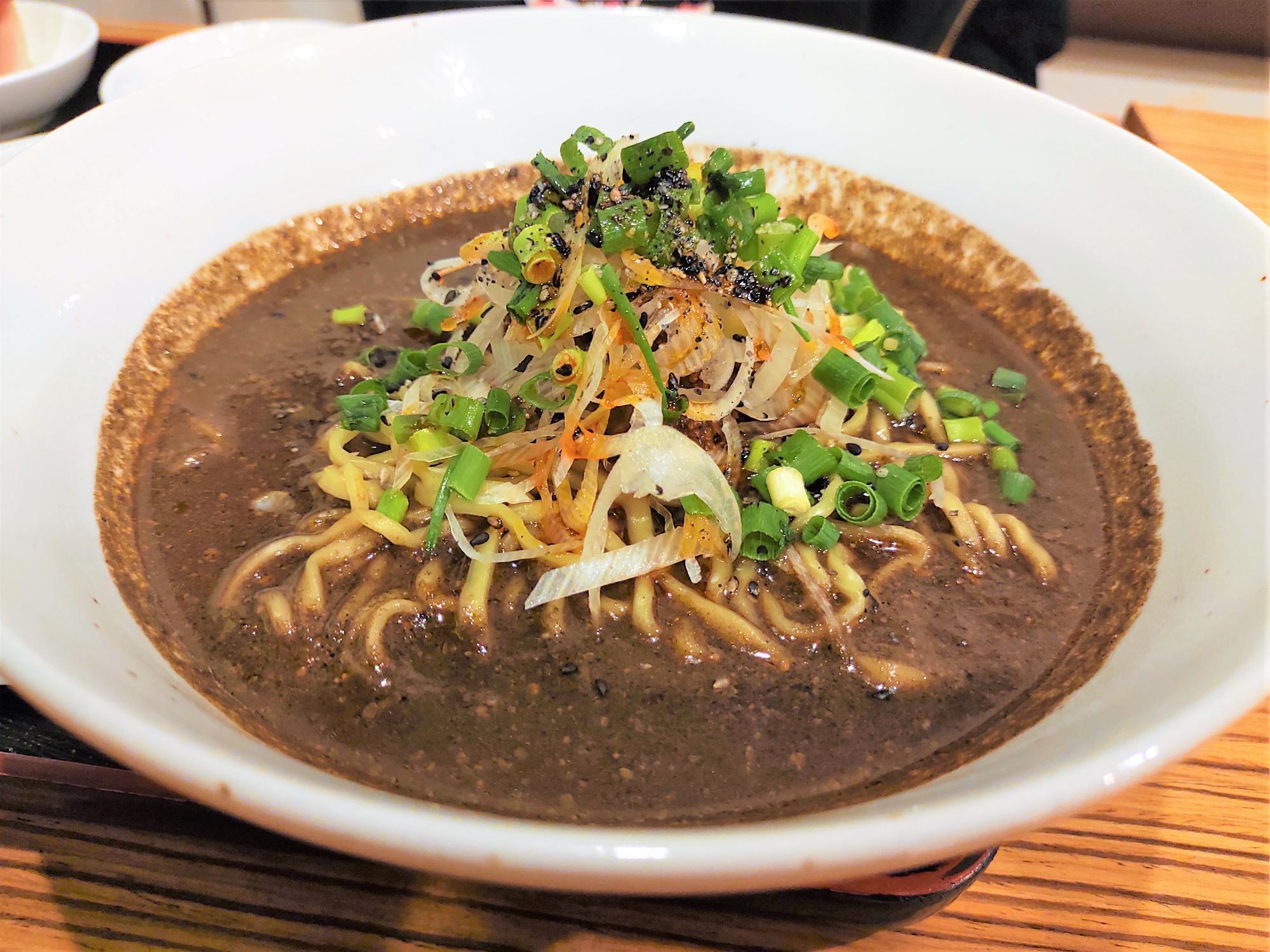 黒胡麻担々麺のアップ写真。濃い色のスープに白ねぎ、青ねぎ、細切り野菜がのった一杯。