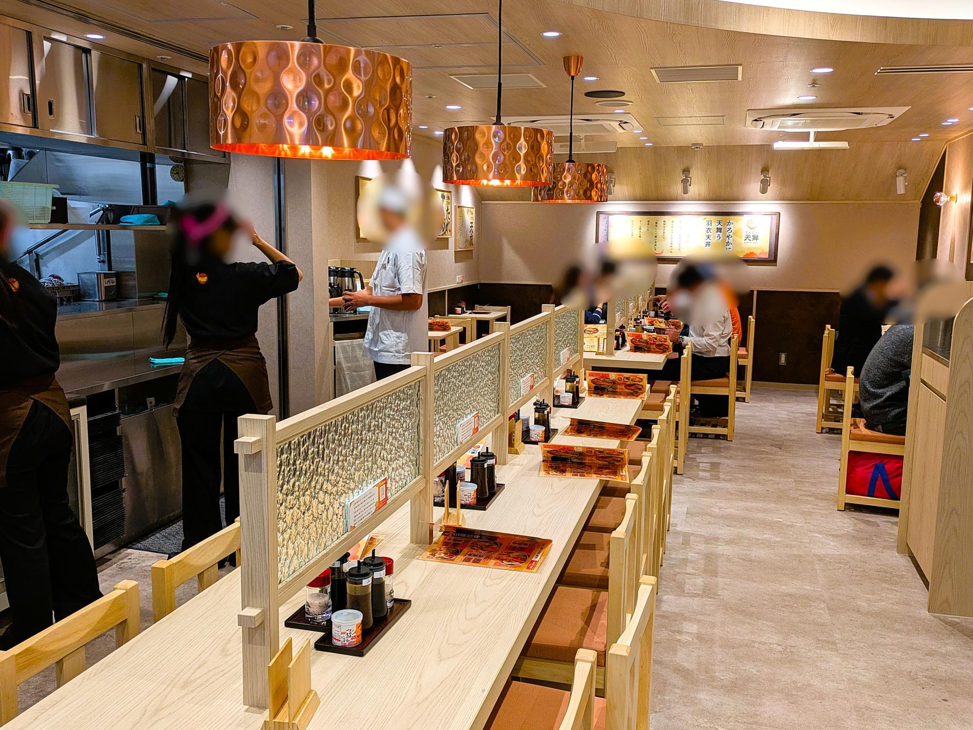名古屋駅の天丼専門店『天舞』の店内。木目のテーブルと仕切りが並ぶ落ち着いた空間で、カウンター奥には調理場が見える。