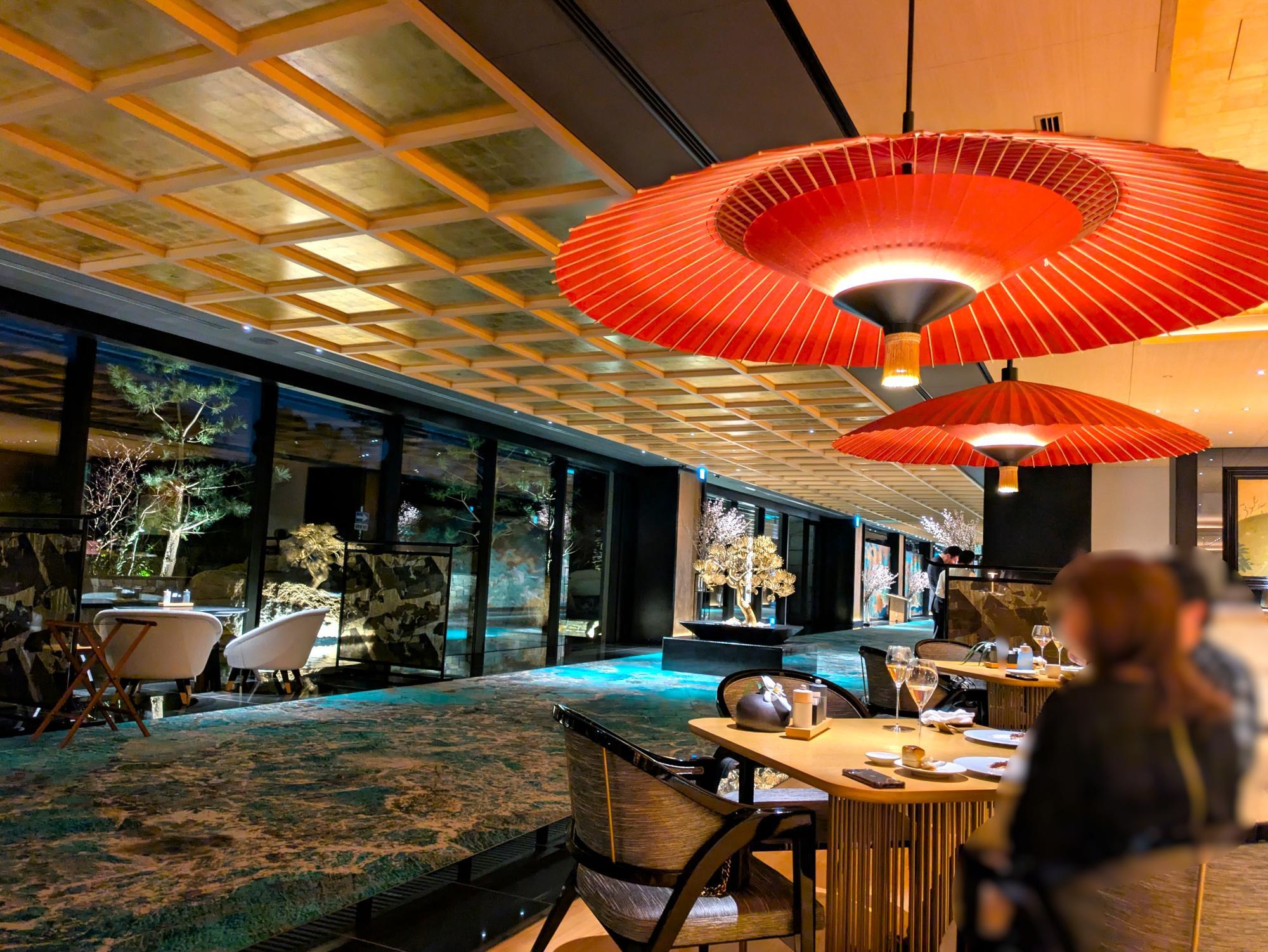 エスパシオ ナゴヤキャッスルのレストラン内観。赤い和傘の照明が灯る上質な空間から、ライトアップされた庭園を望む落ち着いたディナーシーン。