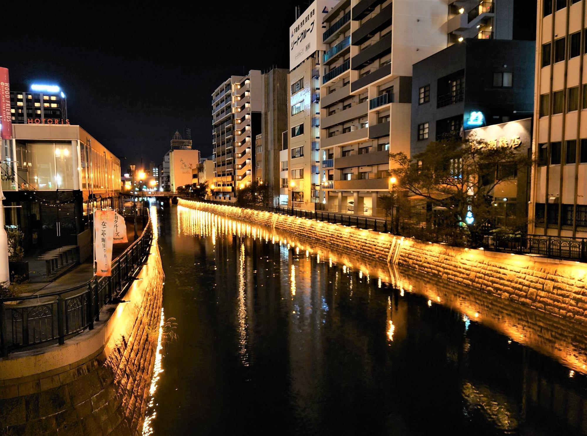夜の堀川に映る街の灯りと、川沿いの建物が並ぶ風景 