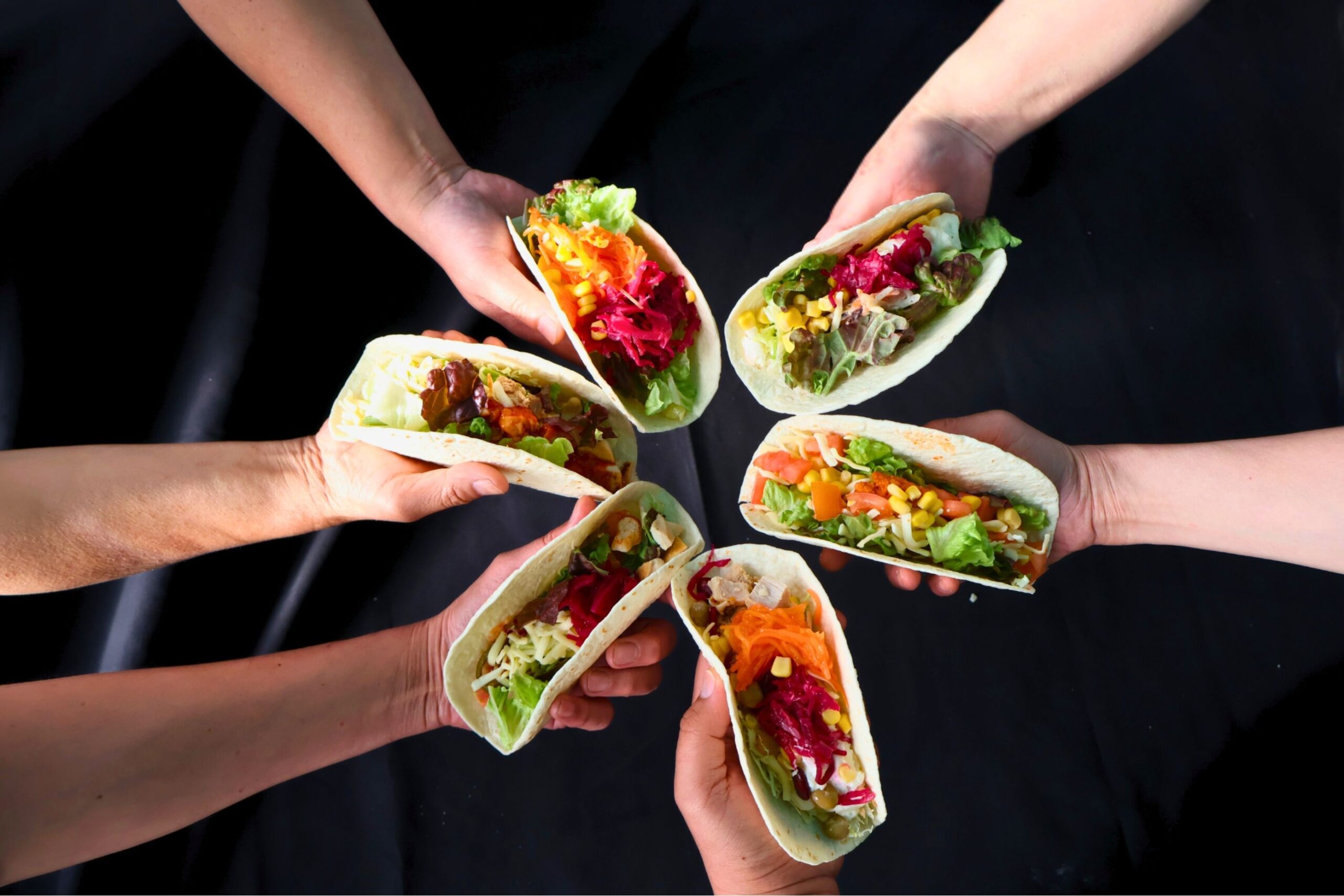 複数のタコスを手に持っている公式イメージ。具材が彩りよく盛り付けられている様子。