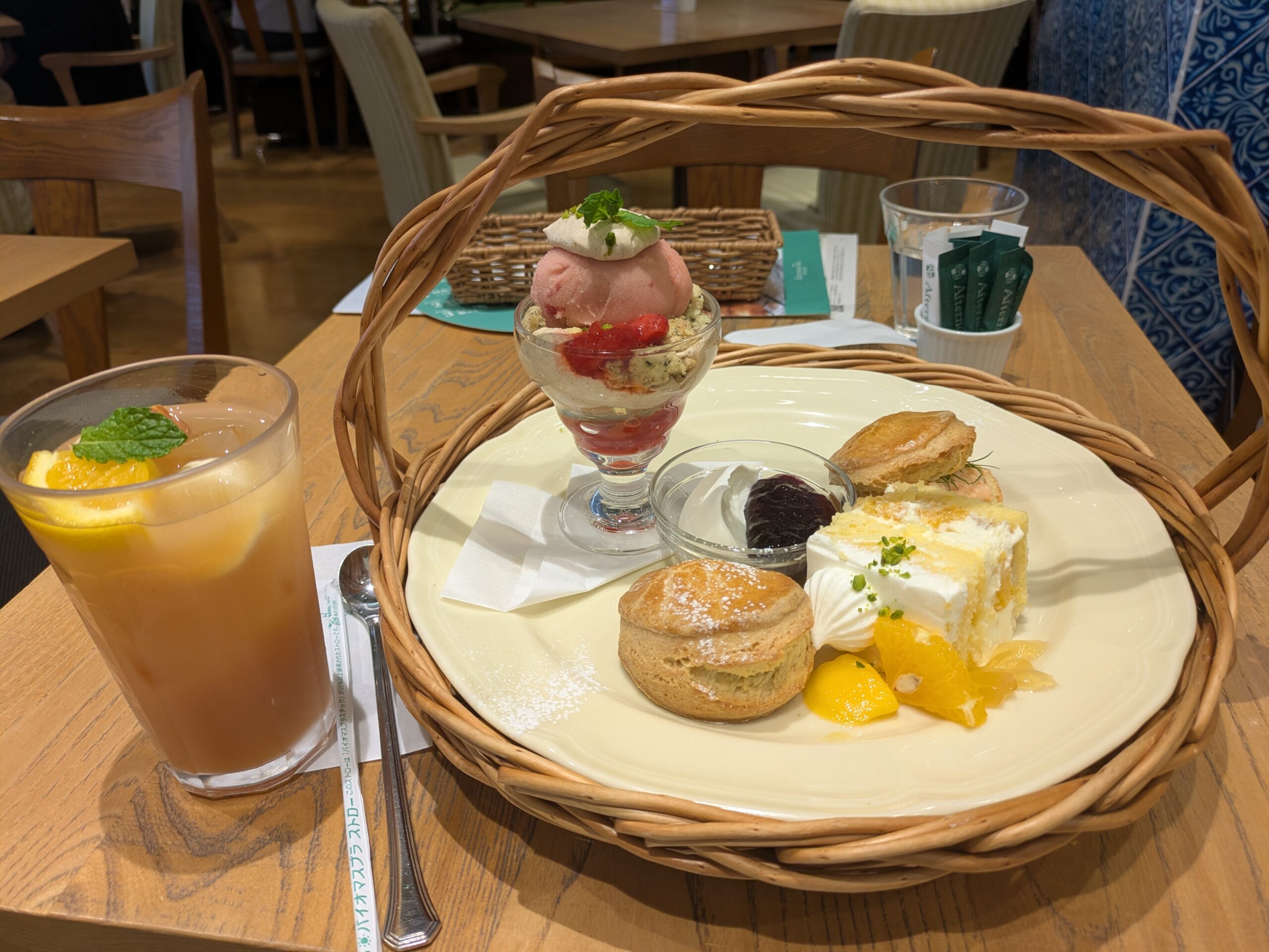 スコーンやパフェ、ケーキが並ぶアフタヌーンティーセットとアイスティーの、落ち着いたカフェテーブル